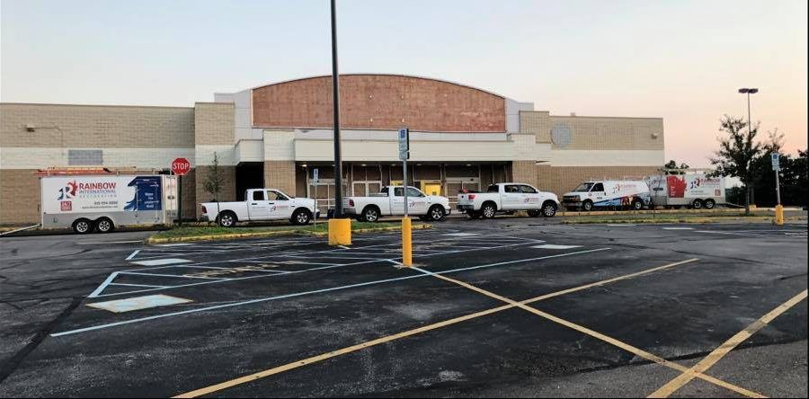 Several Rainbow Restoration trucks are parked in front of a large building.