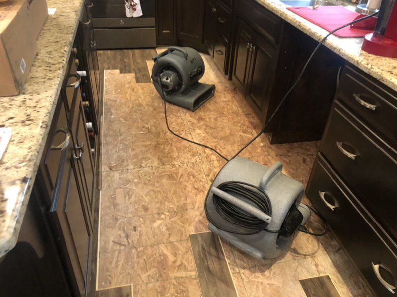 Two industrial fans are sitting on the floor of a kitchen.