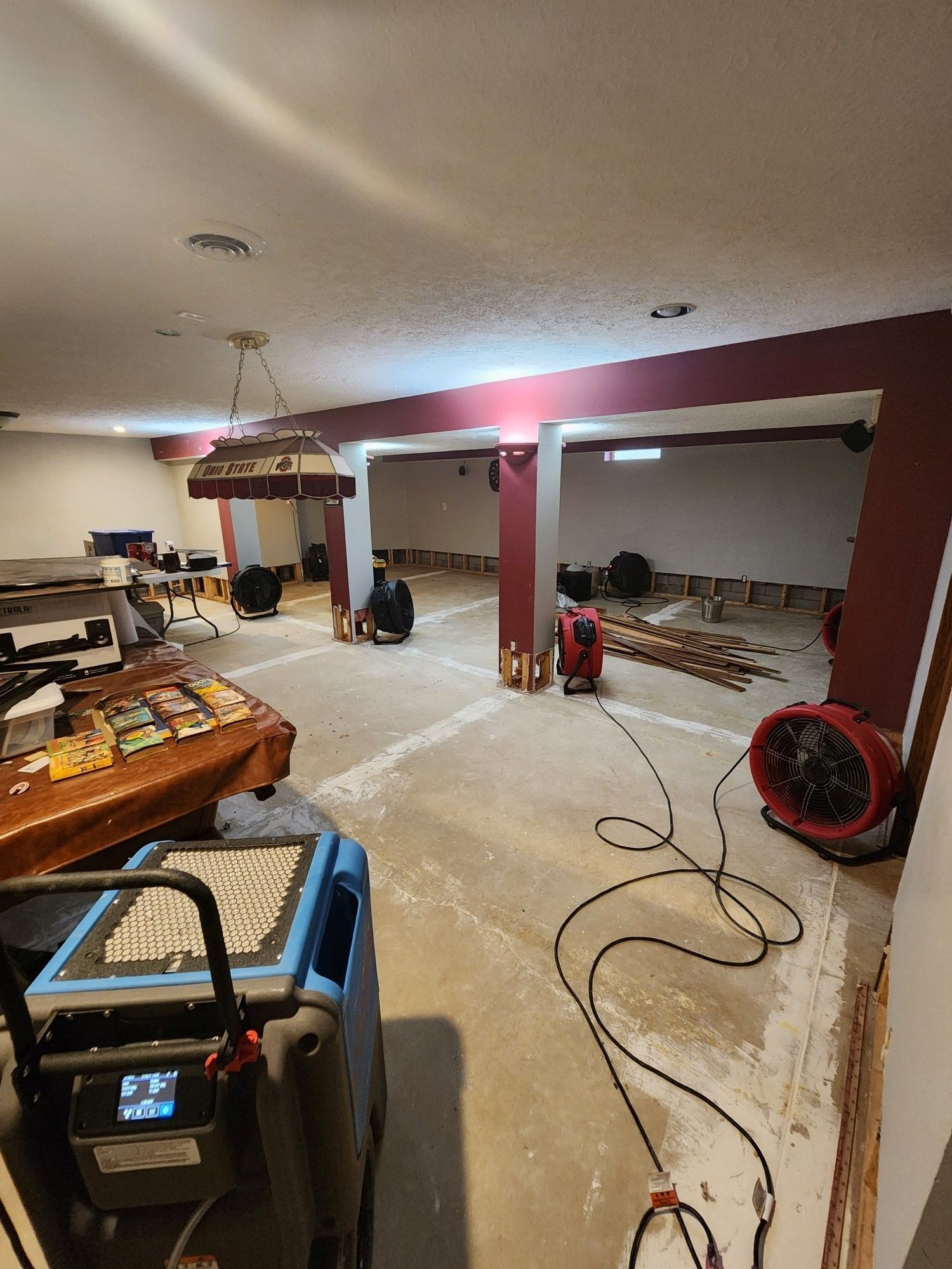A large water damaged room with a pool table and industrial fans on the floor. 