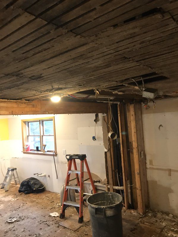 A water damaged room with a ladder, trash can, and damaged ceiling.