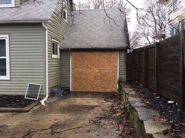 A house with a garage door that has been boarded up because of damage.