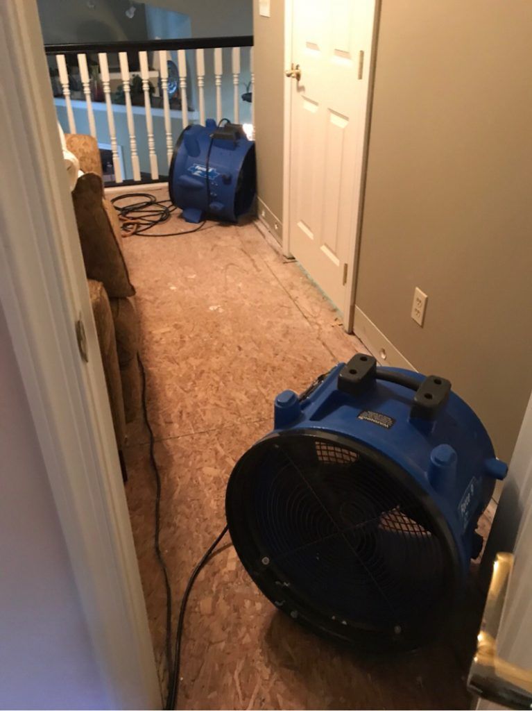 An industrial blue fan is sitting in a hallway next to a door.