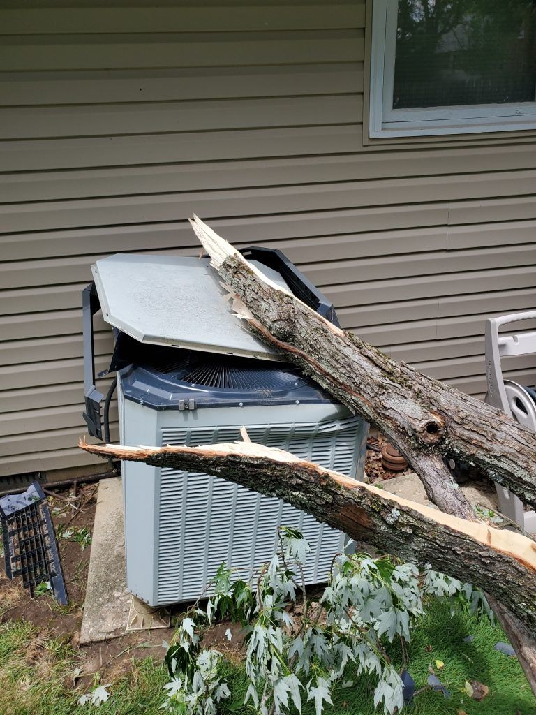 A tree has has fallen on an air conditioner outside of a house.