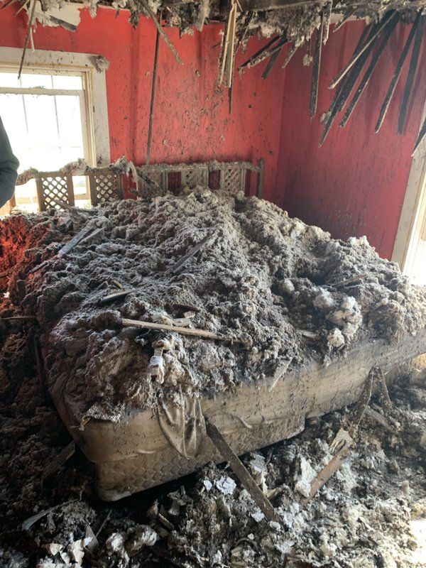 A burnt mattress is sitting on top of a pile of trash in a room.