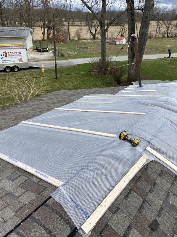 A roof is being covered with plastic and wood with a drill.