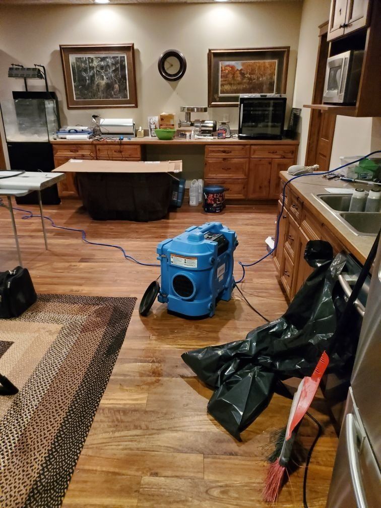 There is an industrial machine on the floor or a room with a rug, table, cabinets, and sinks. 