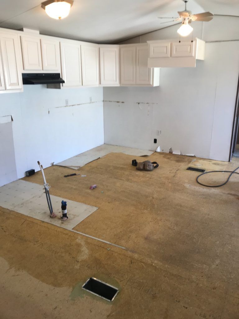 An empty kitchen being repaired containing white cabinets and a ceiling fan.