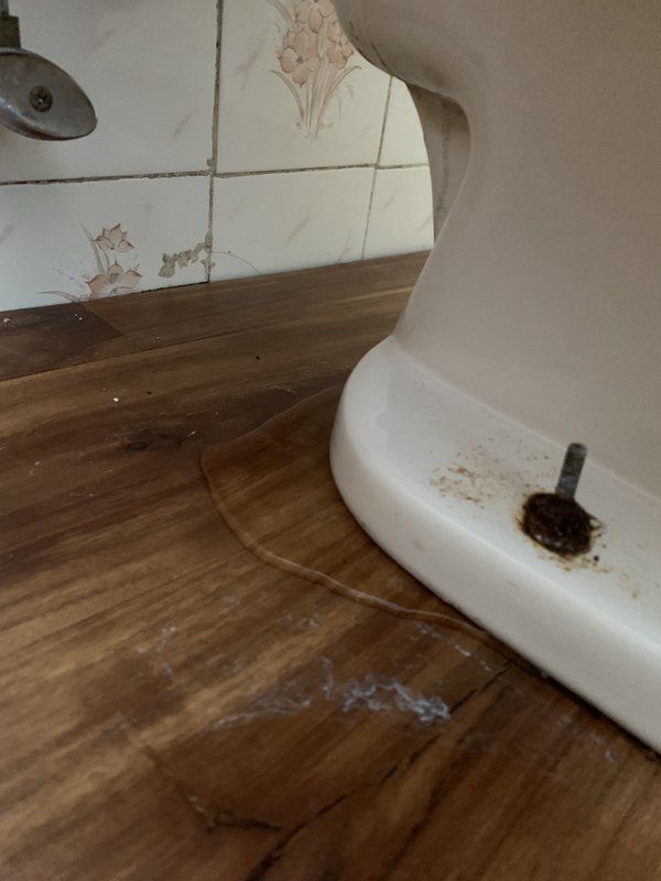 The bottom of a toilet with water coming out of the bottom on a wooden floor. 