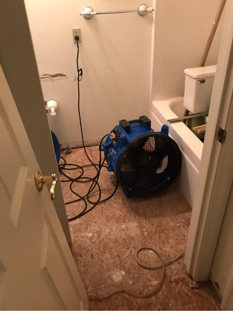 An industrial blue fan is sitting in a bathroom next to a bathtub.