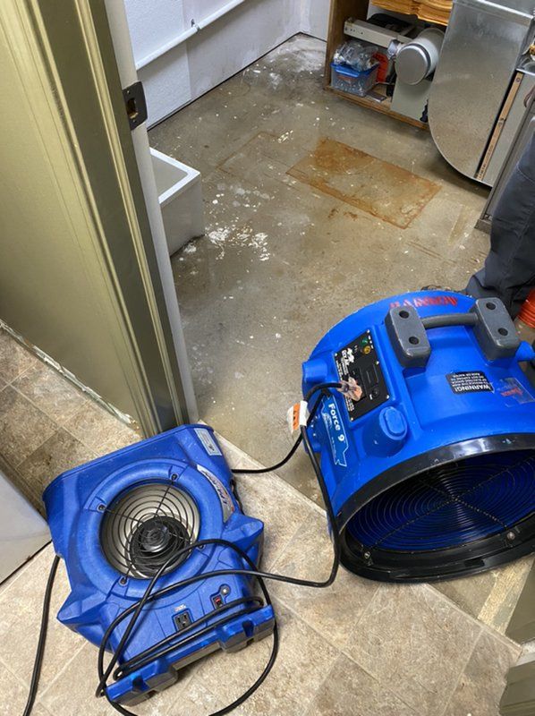 An industrial blue fan is sitting on the floor in a room next to a door.