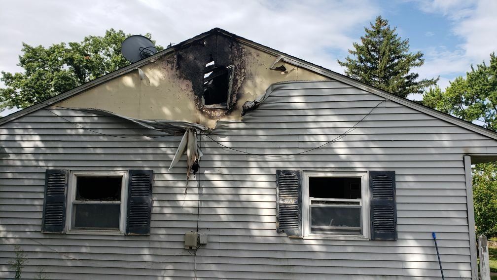 A white house with black shutters has been damaged by a fire.