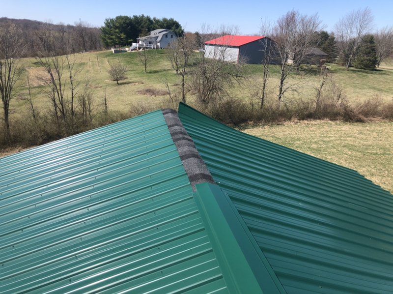 A green metal roof with a red barn in the background.