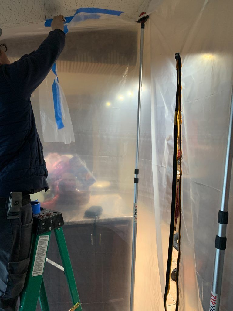 A man is standing on a ladder covering the ceiling with blue tape.