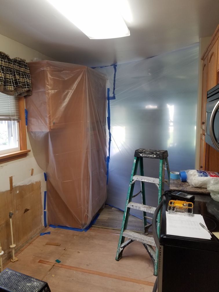 A room that is being repaired with a ladder and a plastic sheet on the wall.