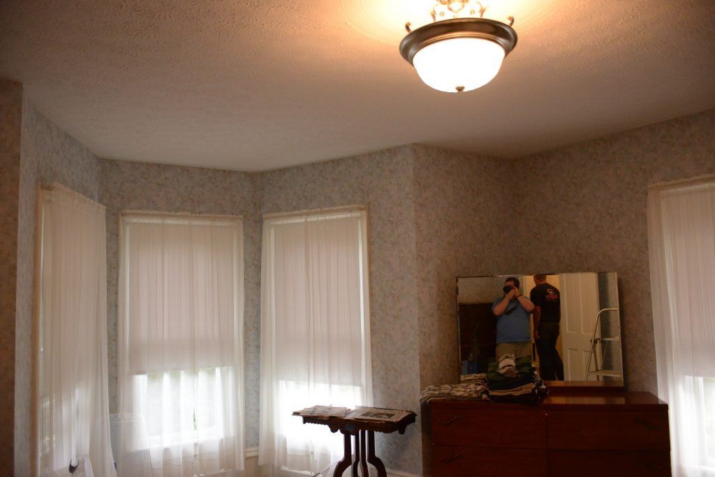 A rom with windows, blinds, and a mirror displaying person taking picture.