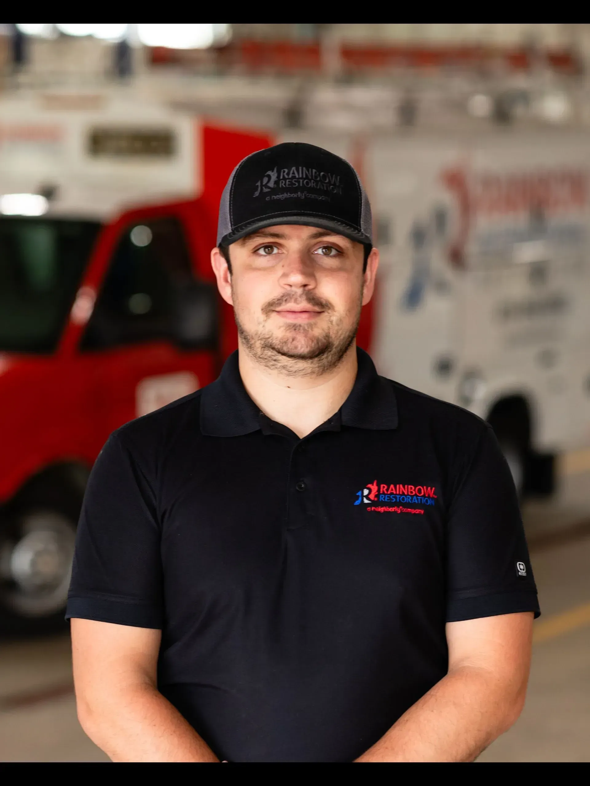 A man with a beard is wearing a black shirt and standing in front of a truck.