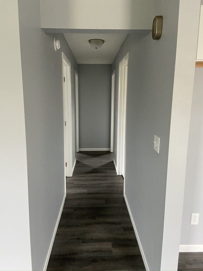 The hallway of a home with gray walls and wooden floors in a house.