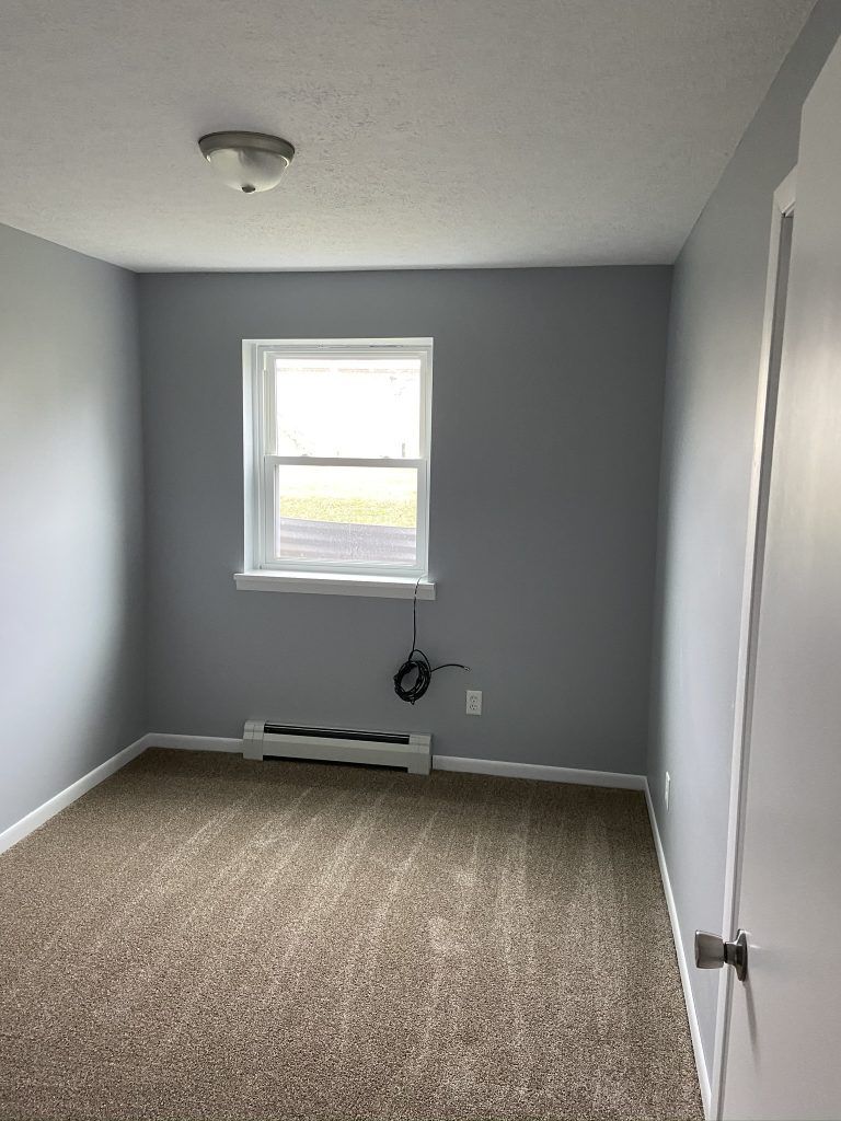 There is a window with black cable hanging from it in a room with a heating register.