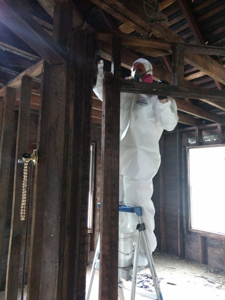 A man in a white suit is standing on a ladder in a room.