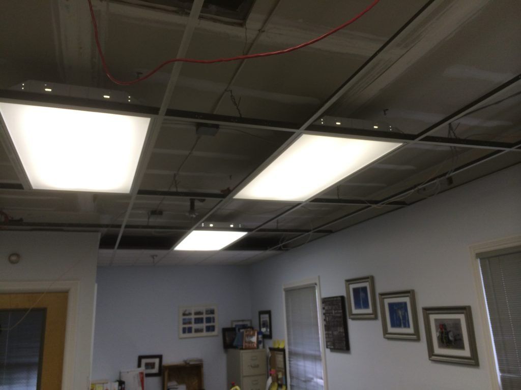 A room with a ceiling that has a lot of lights and missing tiles. 
