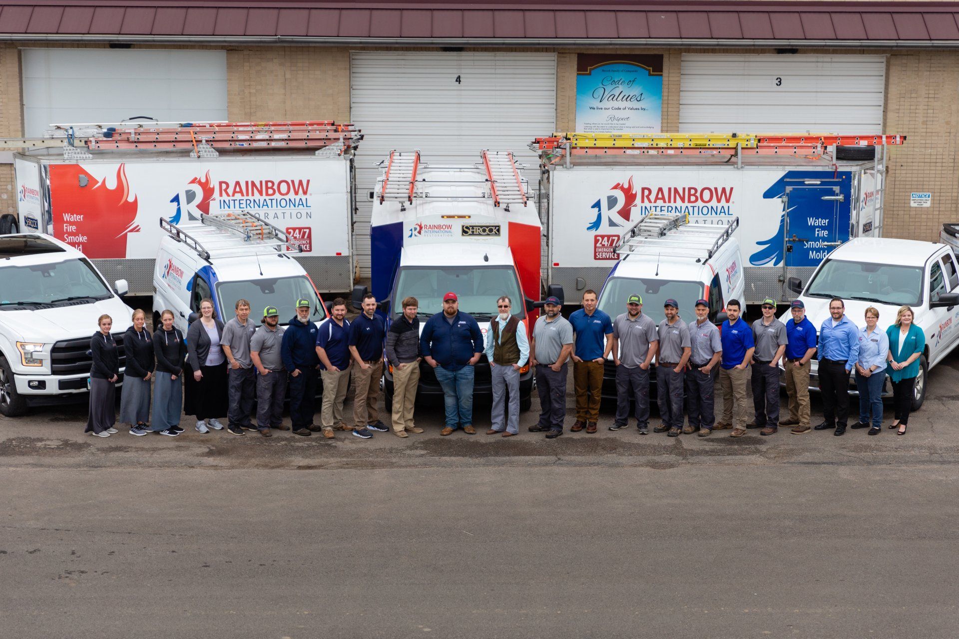 A group of people standing in front of Rainbow Restoration trucks.