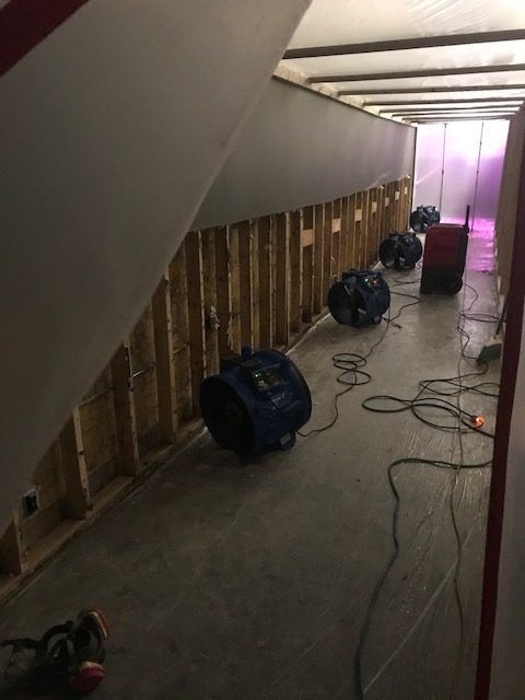 A room with a lot of wires hanging from the ceiling and industrial fans lined up.