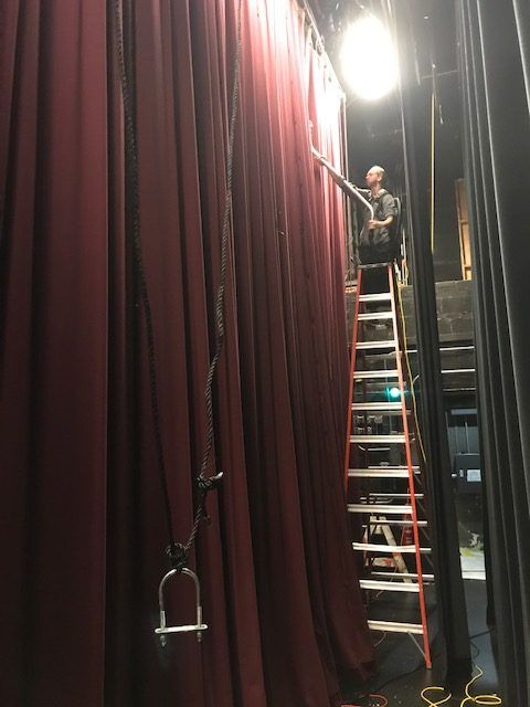 A man standing on a ladder in front of a red curtain.
