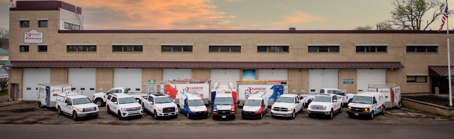 A row of Rainbow Restoration are parked in front of a building.