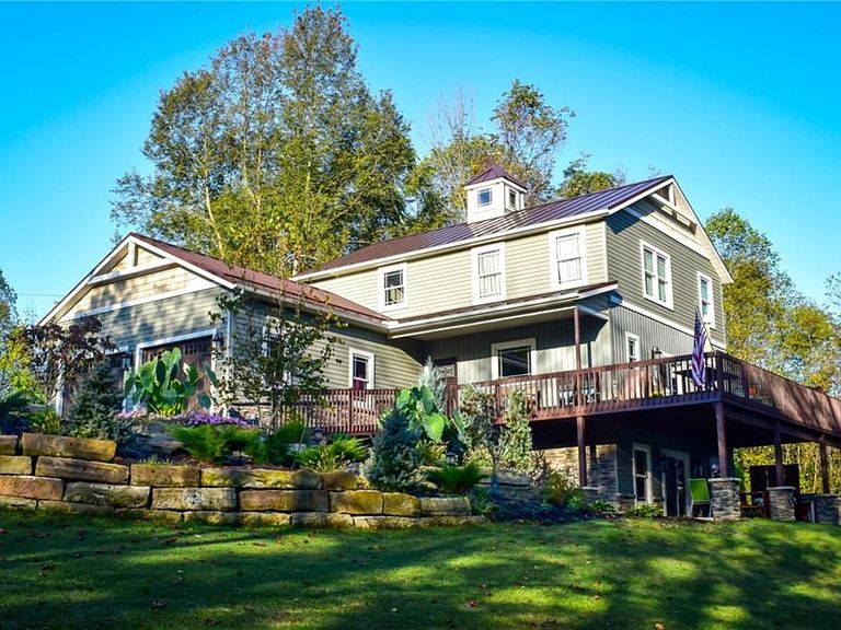 A picture of a large house with a deck taken from the yard surrounded by trees.