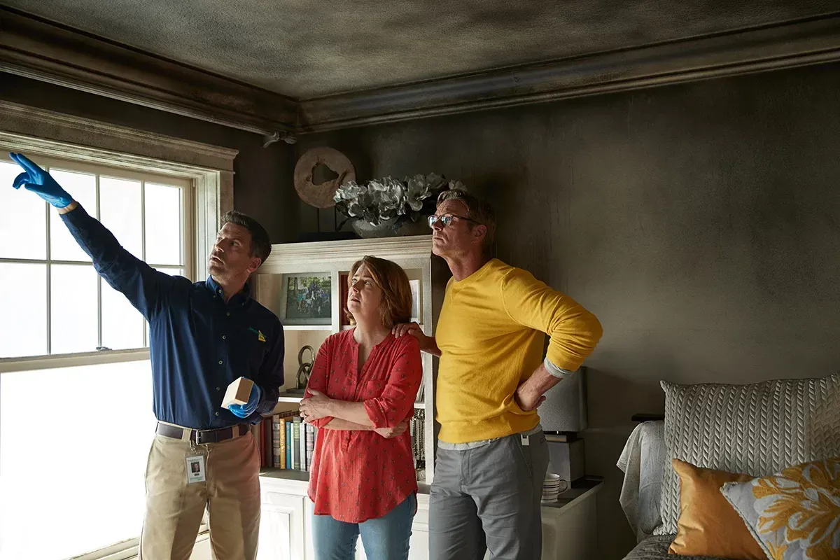 A group of people are standing in a living room looking up at the ceiling.