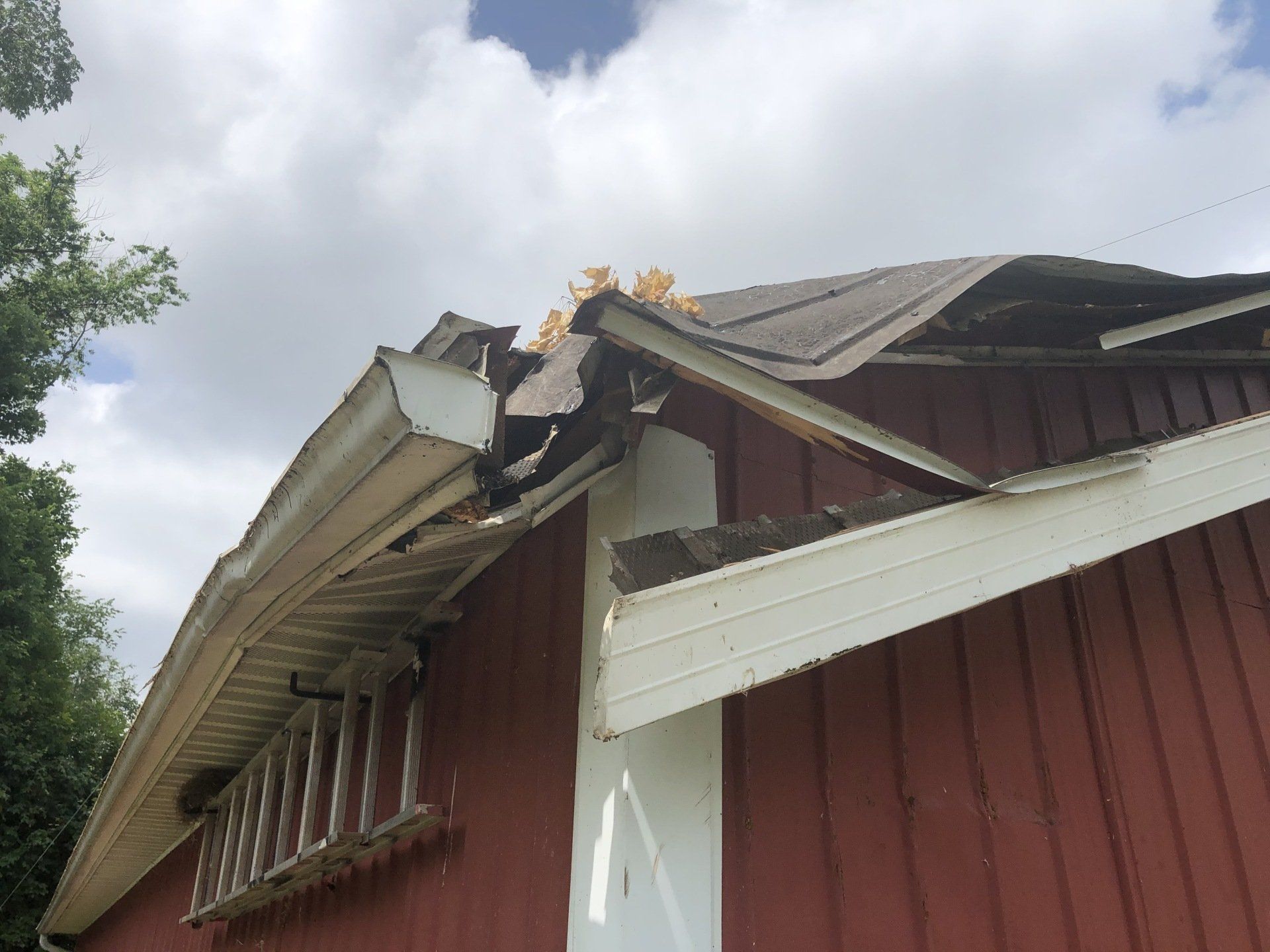 A red barn with a roof that has been damaged by a tree.