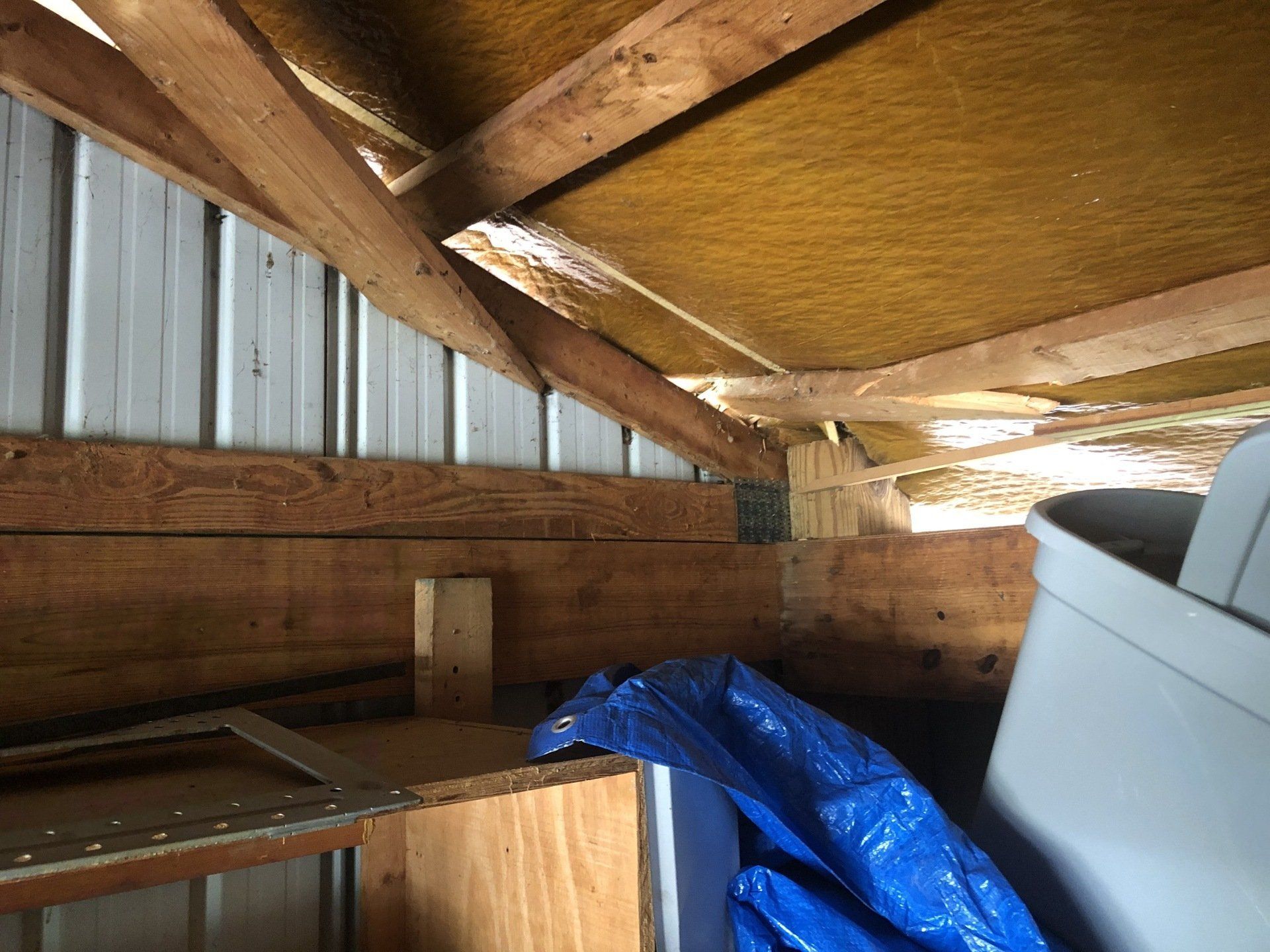 A shed with a blue tarp and a trash can in it.