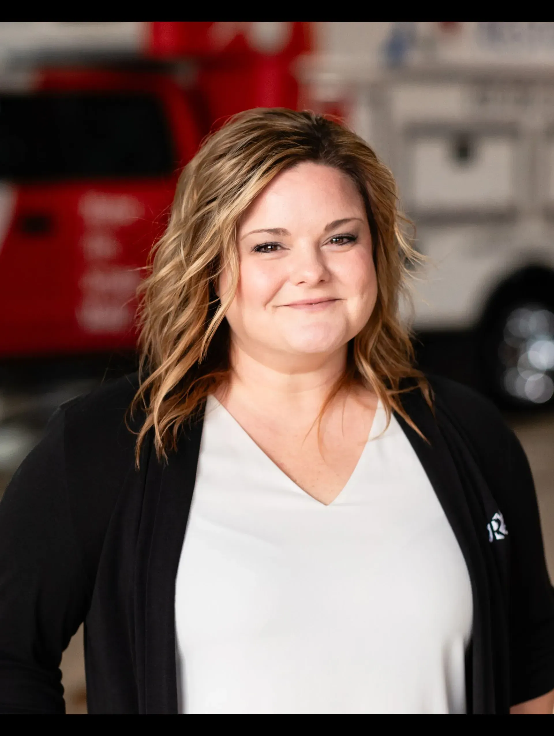 A woman in a white shirt and black cardigan is smiling in front of a red truck.