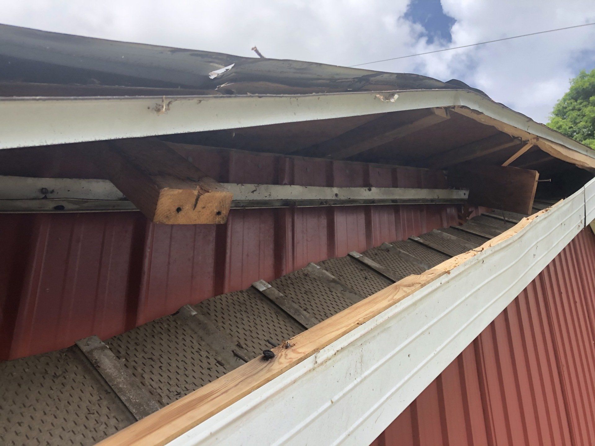 A red building with a white siding and a roof that has been damaged by a tree. 