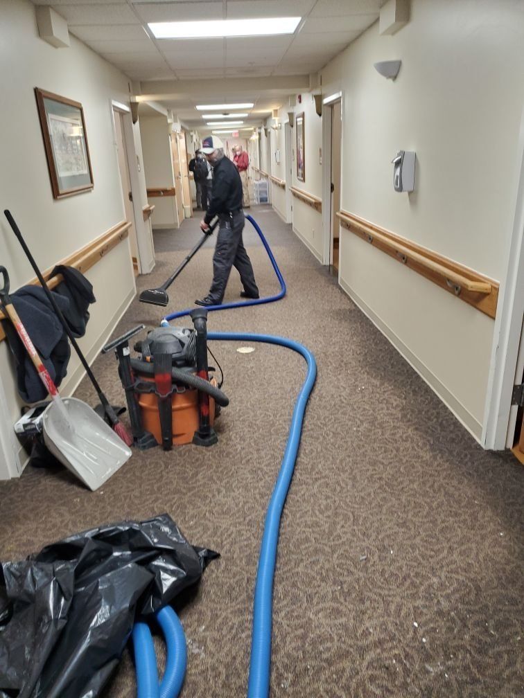 A man is cleaning a hallway with an industrial vacuum cleaner.