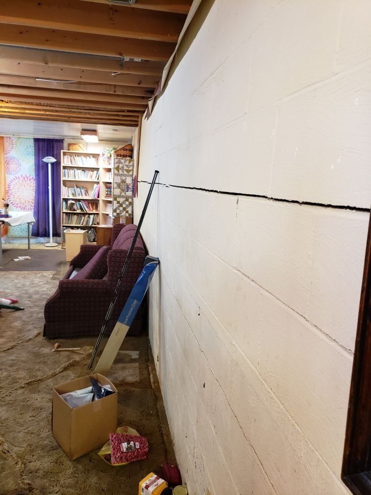 A room in a basement with a couch and bookshelf in as well as a brick structural wall which has been damaged by flood. 
