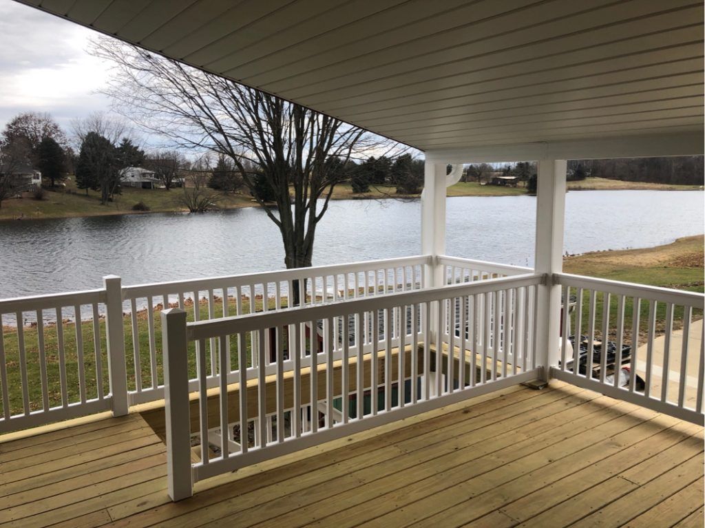 A deck with a white railing and a roof overlooking a lake.