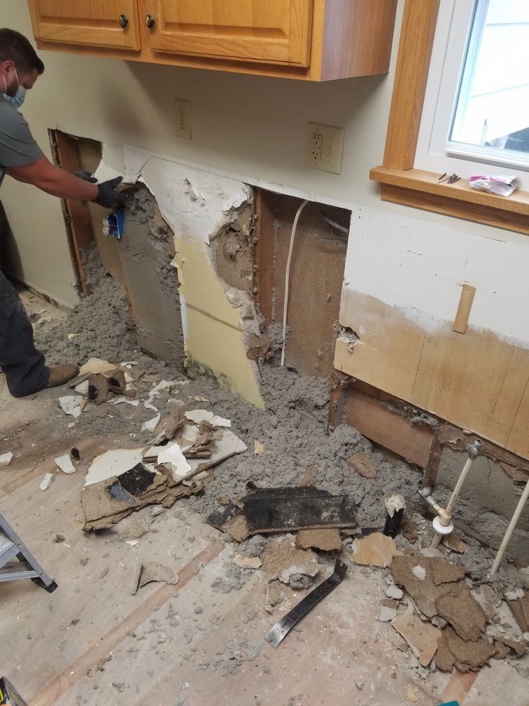 A man is cutting a hole in the wall in a kitchen to repair water damage. 