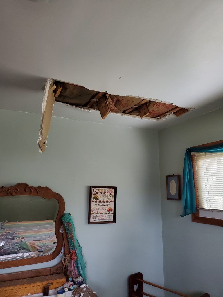 A bedroom with a hole in the ceiling and a picture on the wall and a mirror.