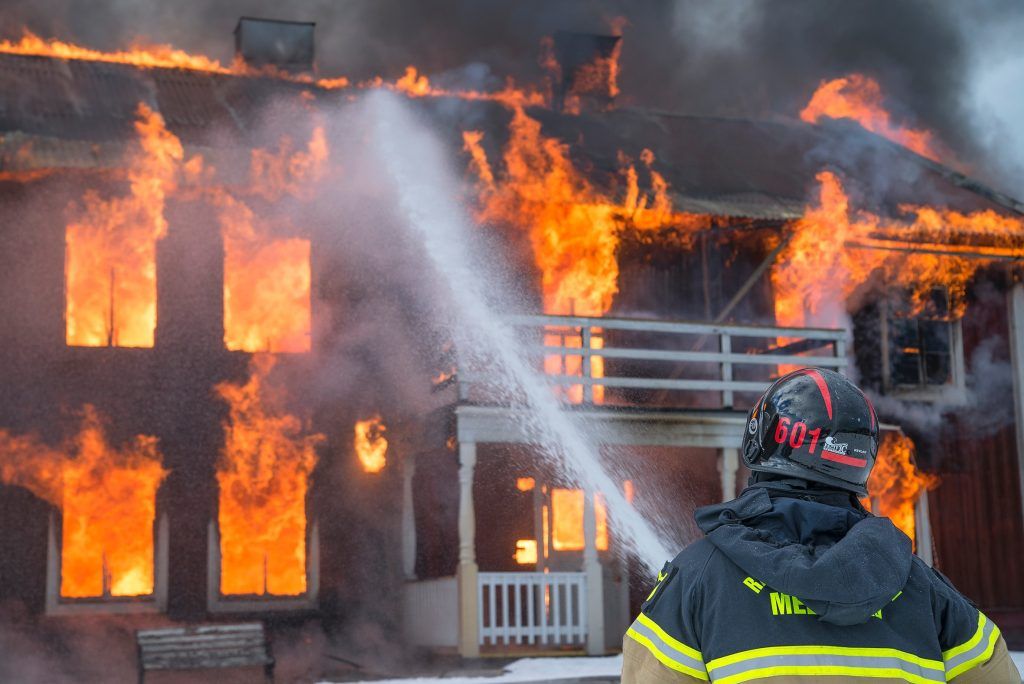 A fireman fighting house fire with water and hose.