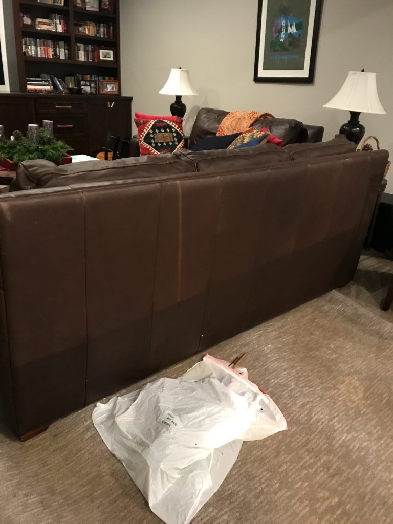 A living room with a brown couch and a white bag on the floor.