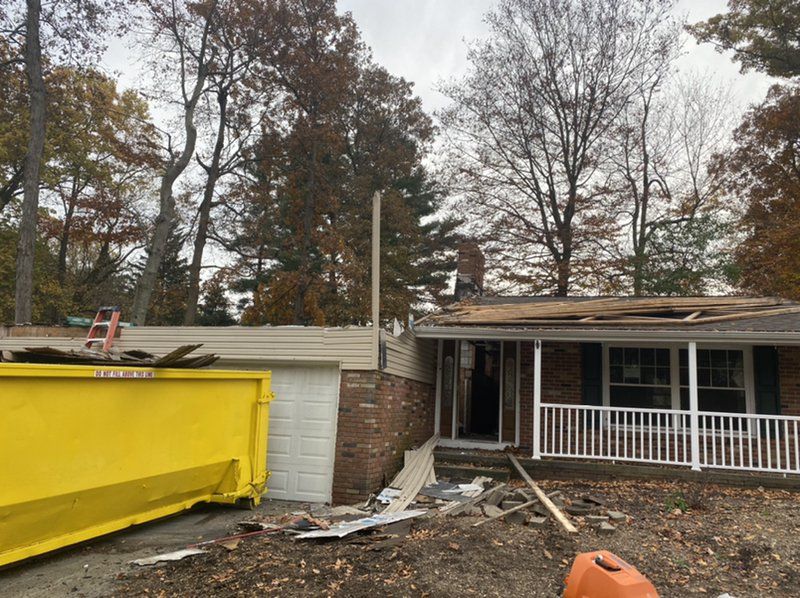 A yellow dumpster is sitting in front of a house that has been damaged..