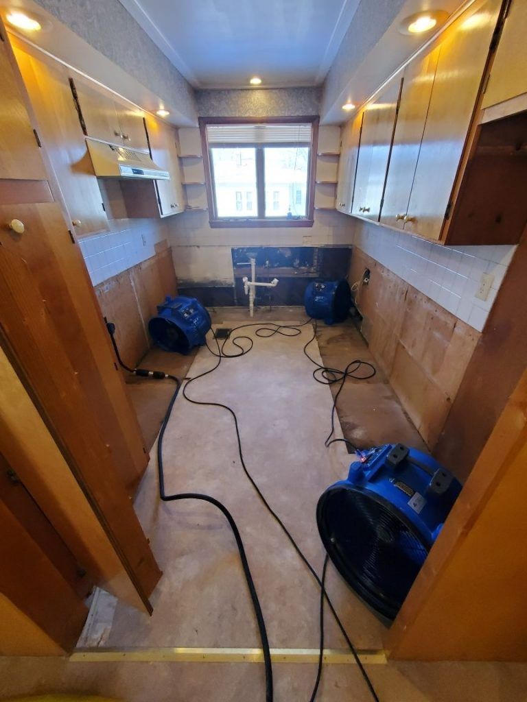 A kitchen with cabinets and industrial drying fans on the floor. 