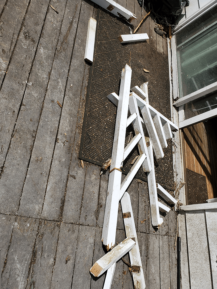 Broken white railing laying on wooden deck caused by a falling tree. 