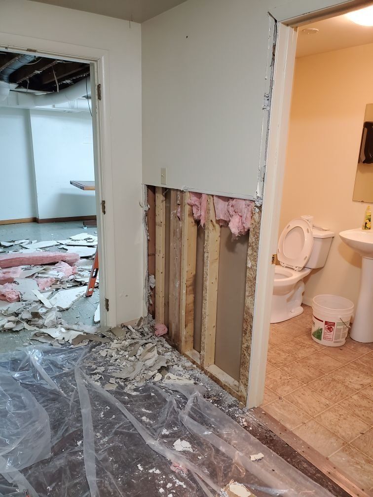 A damaged bathroom with a toilet , sink and a hole in the wall.