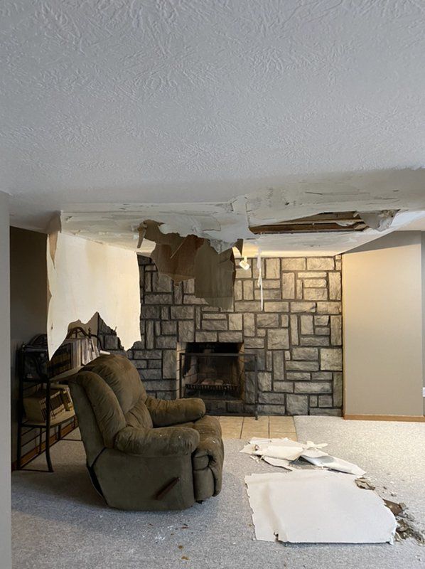 A living room with a brick fireplace and a recliner and fire damaged ceiling. 