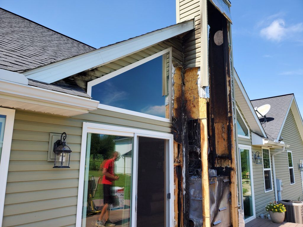 A man is standing in front of a house that has been damaged by a fire.