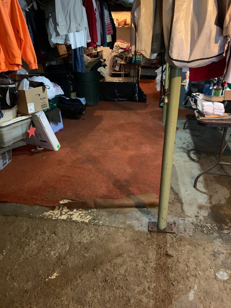 A room with a lot of clothes hanging on clotheslines and boxes on the floor.