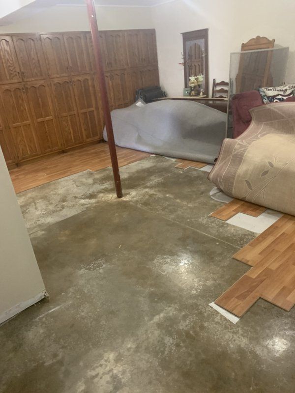 A room with wooden floors on top of a concrete floor in water damaged basement. 