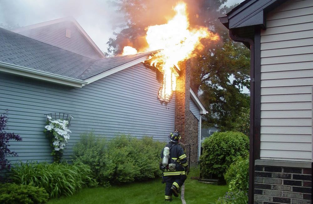 A house with a fire beside the chimney and a firefighter. 